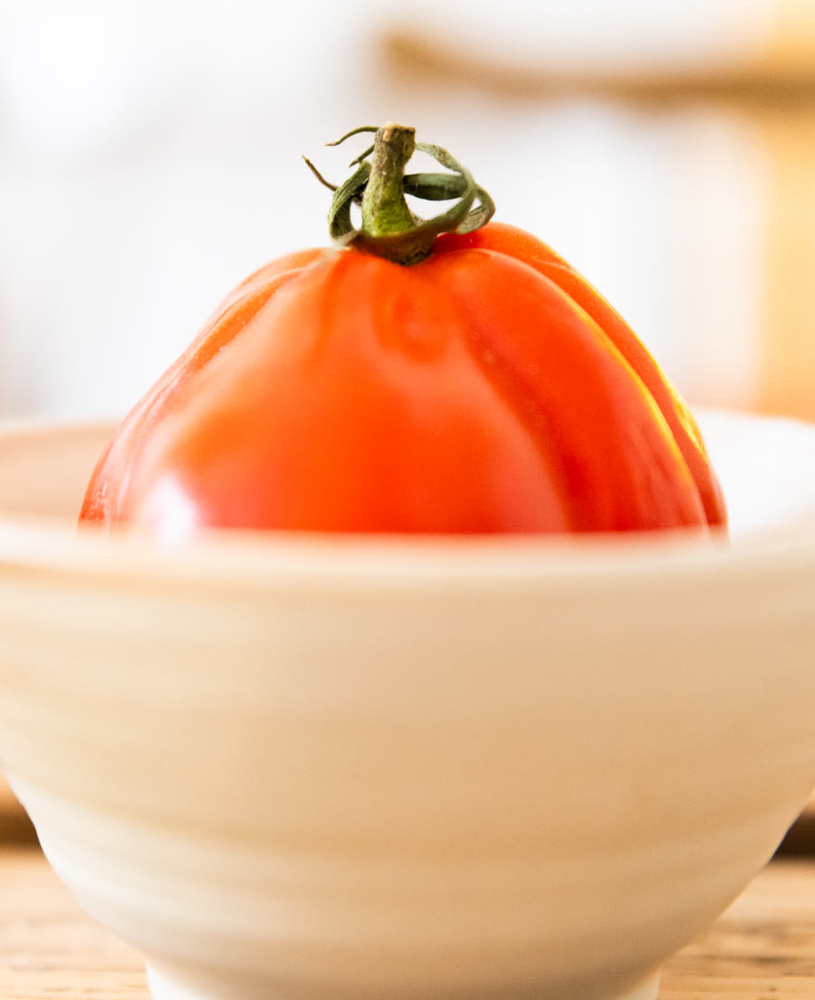 Tomate cœur de bœuf posée en équilibre sur un bol blanc, gros plan