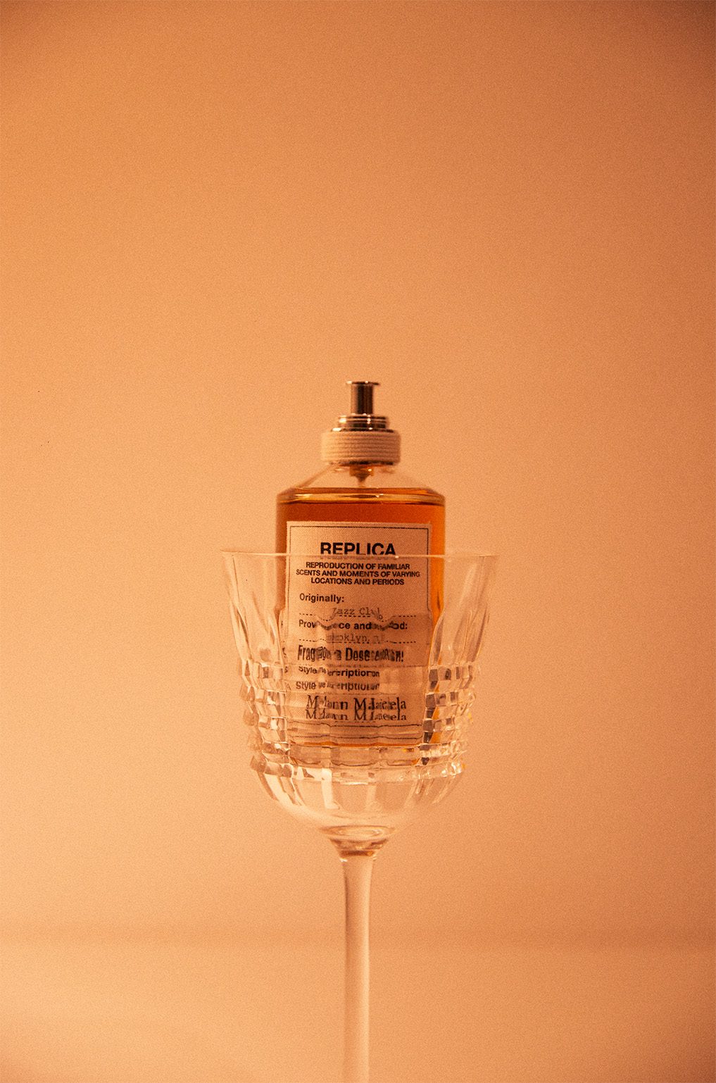 Nature morte : flacon de parfum posé dans un verre en cristal taillé, fond orangé