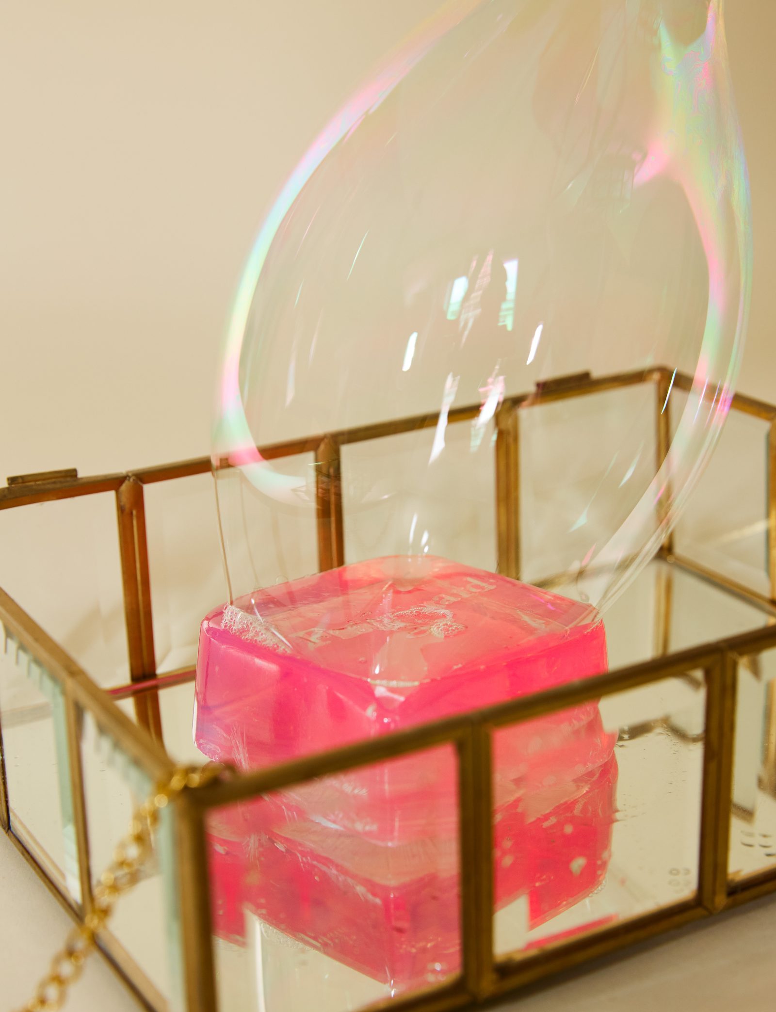 Savon rose dans une boîte en verre et laiton, bulle de savon irisée au-dessus