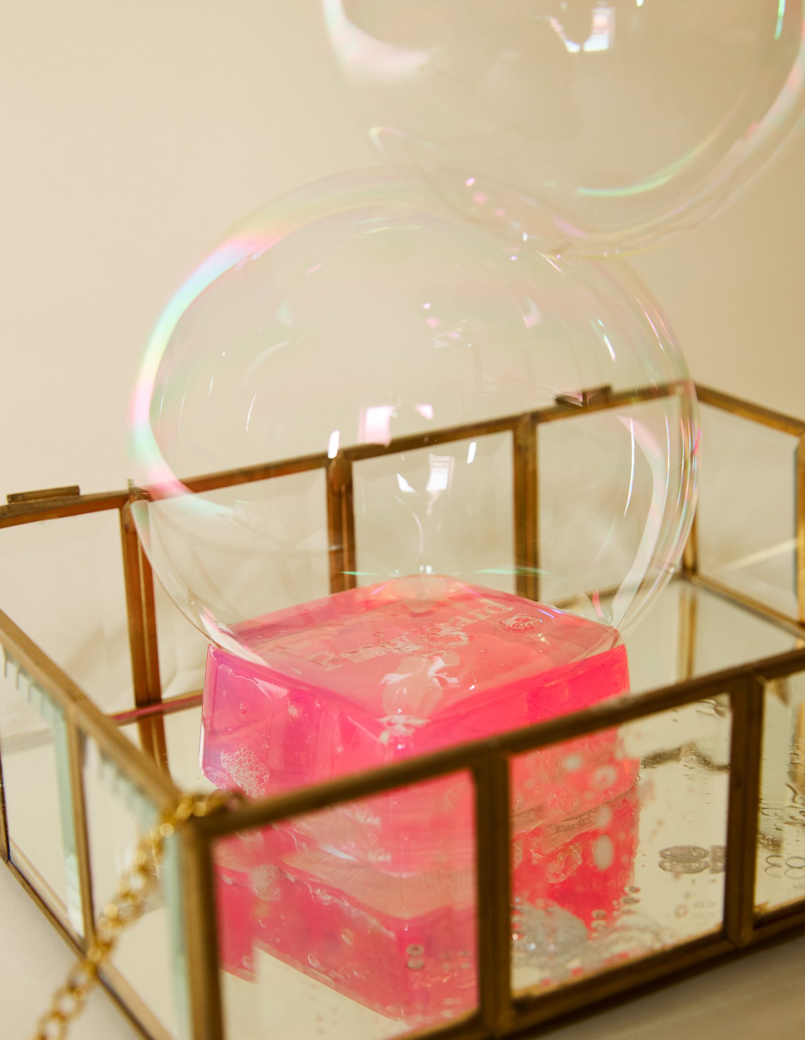 Savon rose dans une boîte en verre et laiton, bulle irisée, cadrage resserré