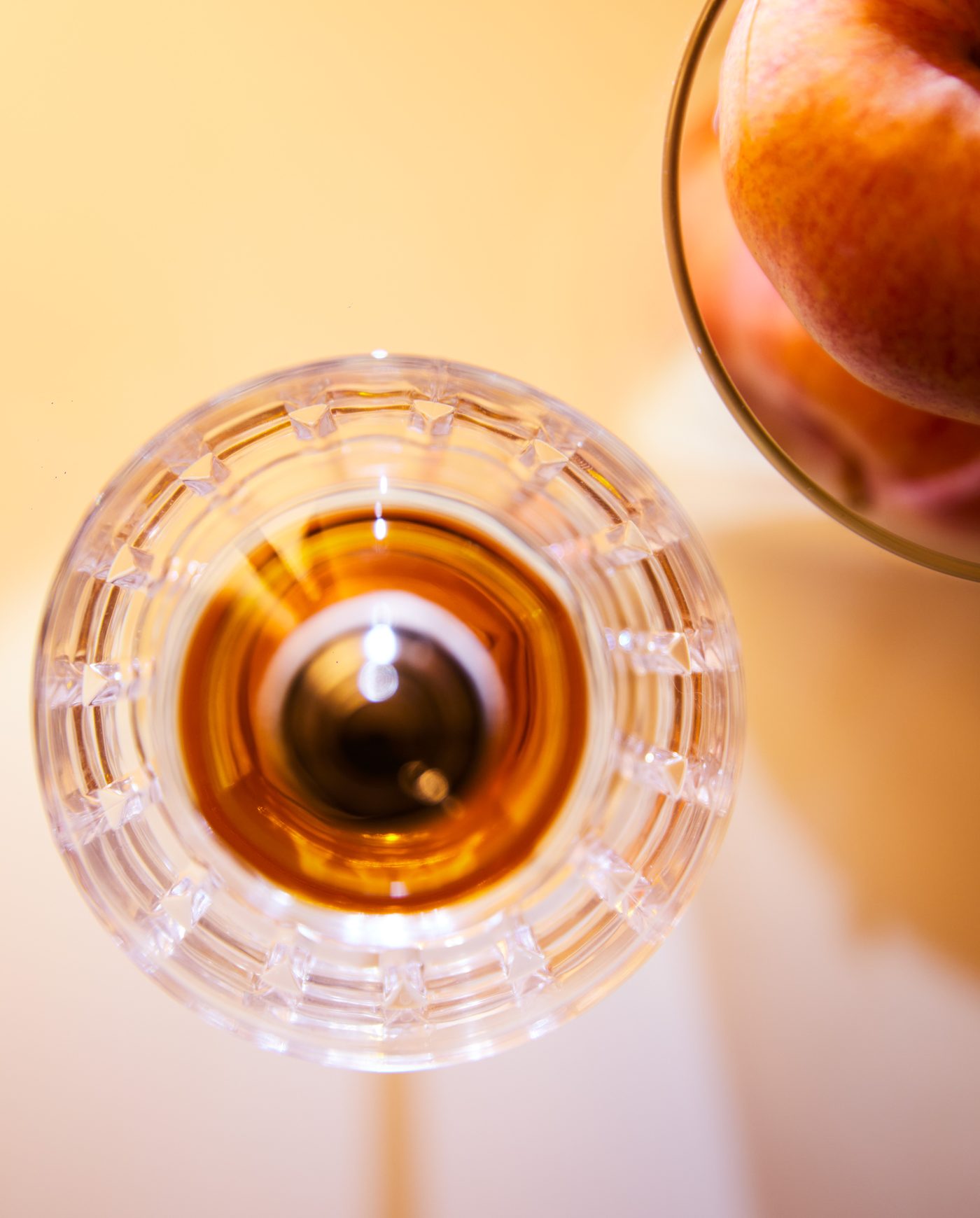 Verre en cristal taillé vu du dessus, liquide ambré, fond crème