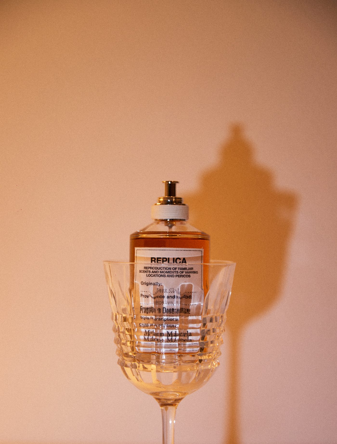 Flacon de parfum dans un verre en cristal, ombre portée nette sur fond rosé