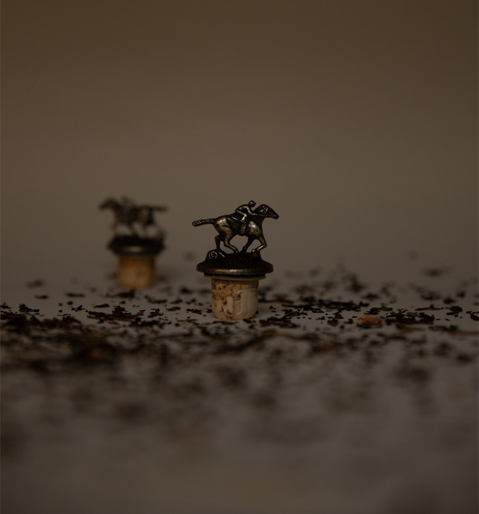 Deux bouchons surmontés de chevaux miniatures sur un lit de grains, fond sombre
