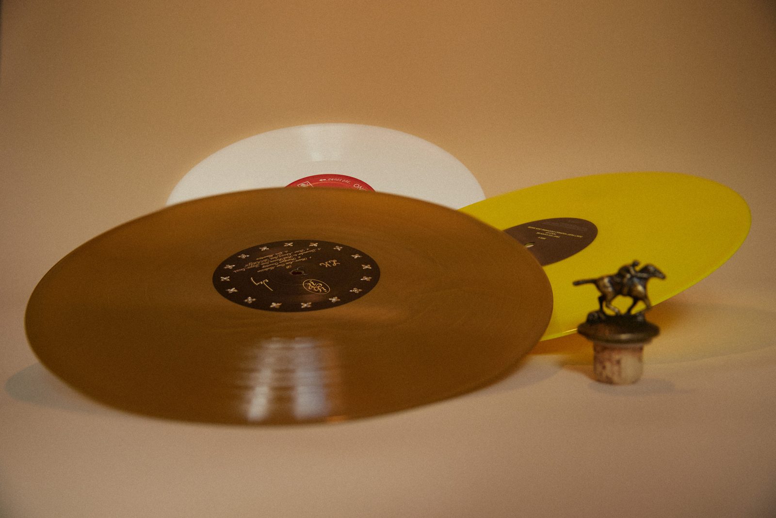 Disques vinyles dorés et blanc et bouchon à tête de cheval, fond crème