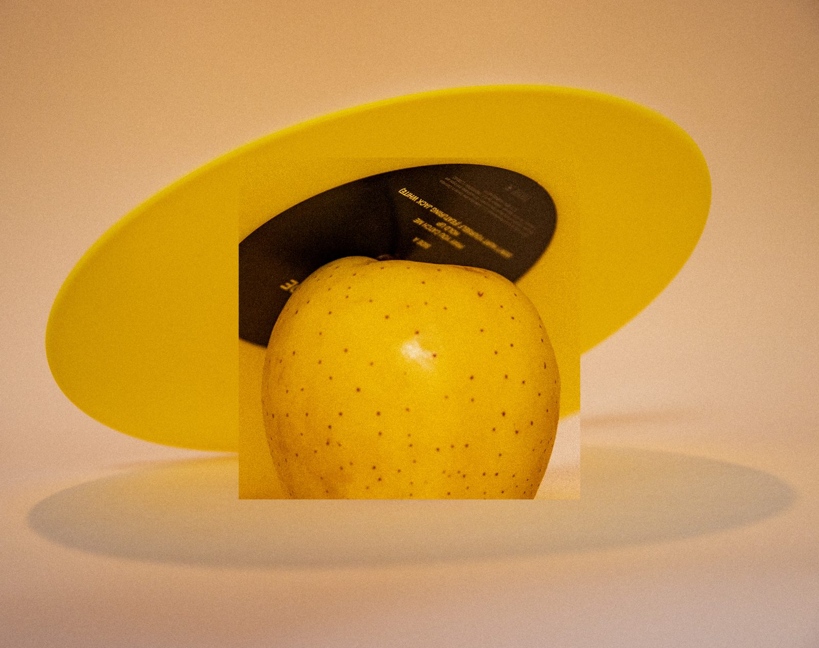 Pomme jaune devant un disque vinyle noir et un disque jaune, fond crème