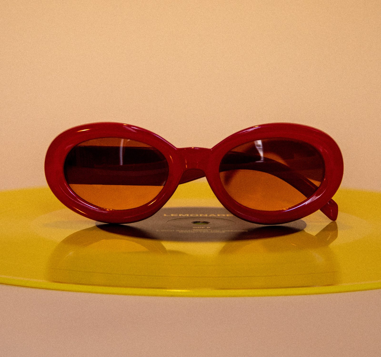 Lunettes de soleil rouges posées sur un vinyle jaune, fond crème