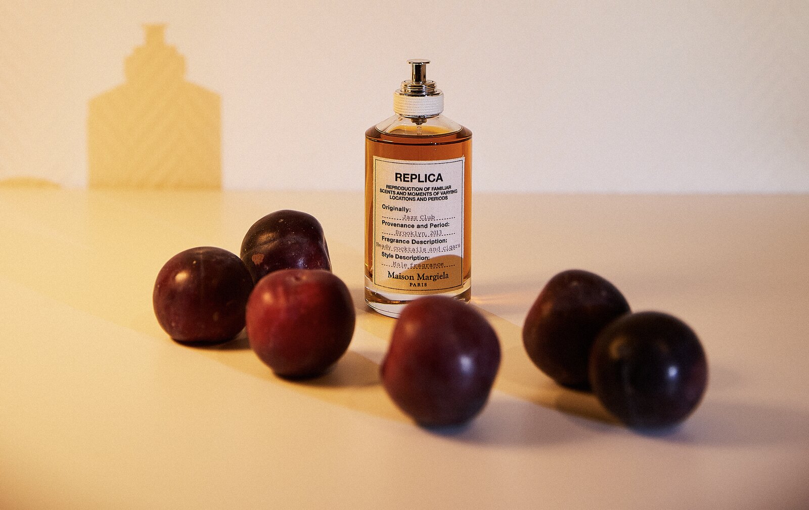 Packshot : flacon de parfum entouré de prunes noires sur fond beige